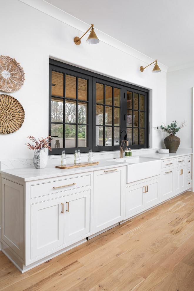 This is an example of a traditional kitchen in Charlotte with a belfast sink, beaded cabinets, white cabinets, engineered stone countertops, white splashback, engineered quartz splashback, coloured appliances, light hardwood flooring, an island, brown floors and white worktops.