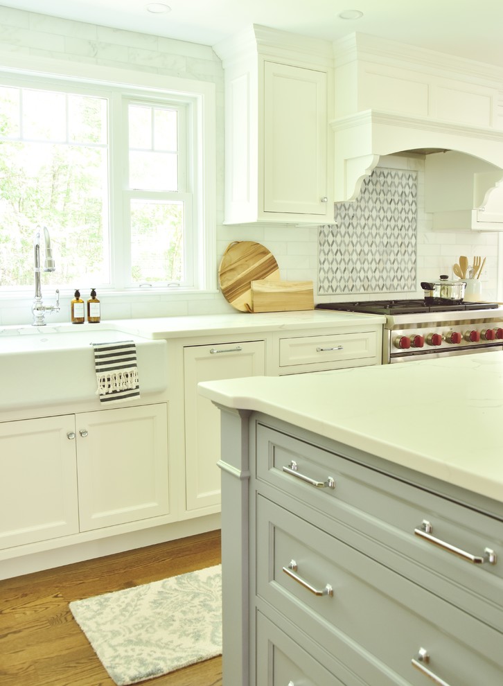 This is an example of a traditional kitchen in Boston with a farmhouse sink, beaded inset cabinets, quartz benchtops, white splashback, marble splashback, stainless steel appliances, dark hardwood floors, with island and white benchtop.