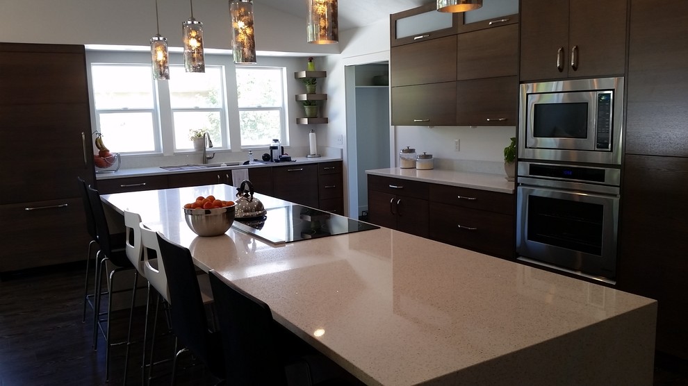 Inspiration for a mid-sized contemporary l-shaped eat-in kitchen in Orange County with a drop-in sink, flat-panel cabinets, dark wood cabinets, solid surface benchtops, white splashback, stone slab splashback, stainless steel appliances, dark hardwood floors and with island.
