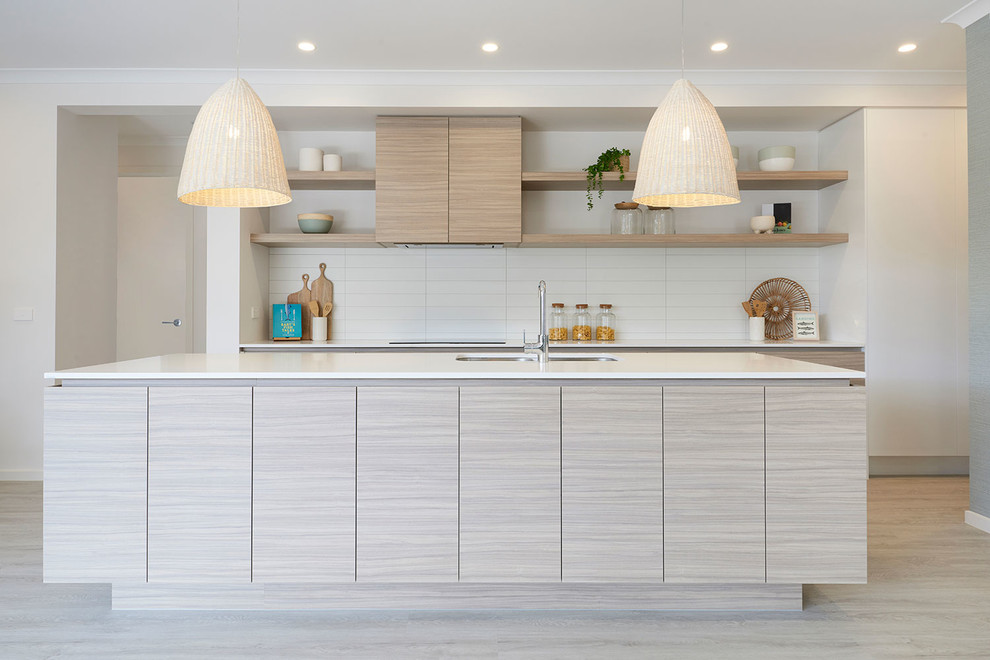Beach style galley kitchen in Melbourne with an undermount sink, flat-panel cabinets, light wood cabinets, white splashback, light hardwood floors, with island, beige floor and white benchtop.