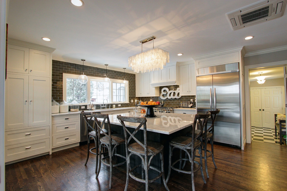 Large transitional l-shaped dark wood floor enclosed kitchen photo in Denver with an undermount sink, shaker cabinets, white cabinets, marble countertops, brown backsplash, subway tile backsplash, stainless steel appliances and an island