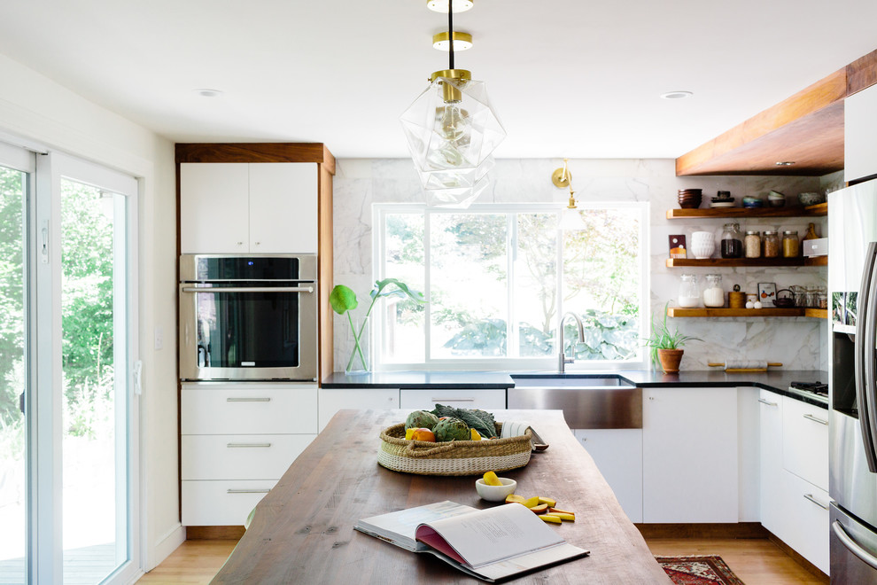 This is an example of a small contemporary l-shaped eat-in kitchen in Boston with a farmhouse sink, flat-panel cabinets, white cabinets, soapstone benchtops, white splashback, stone tile splashback, stainless steel appliances, light hardwood floors and with island.