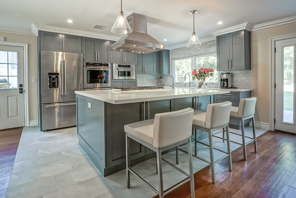 Photo of a large transitional l-shaped open plan kitchen in Los Angeles with a farmhouse sink, shaker cabinets, grey cabinets, quartz benchtops, grey splashback, marble splashback, stainless steel appliances, porcelain floors, with island and white floor.