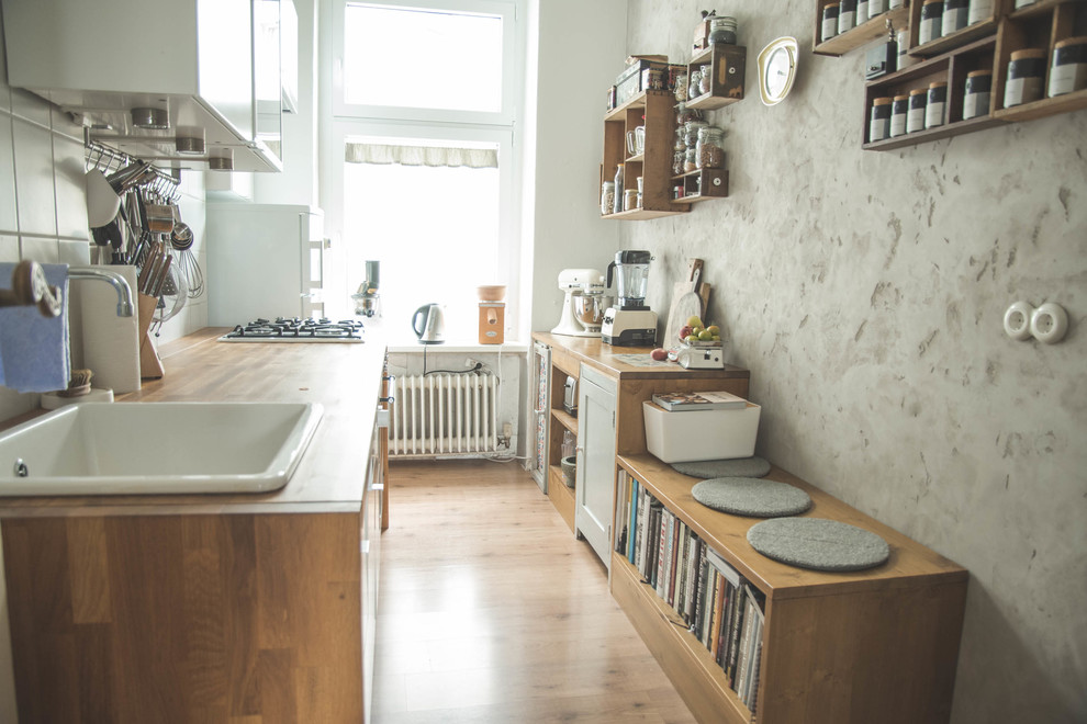 Photo of a mid-sized eclectic single-wall separate kitchen in Berlin with a drop-in sink, wood benchtops, white splashback, ceramic splashback, white appliances, light hardwood floors and no island.
