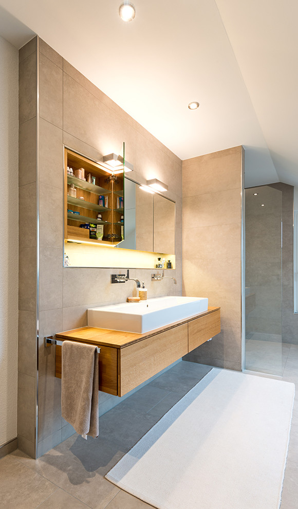 This is an example of a contemporary bathroom in Berlin with flat-panel cabinets, medium wood cabinets, a curbless shower, beige tile, a trough sink, wood benchtops and brown benchtops.