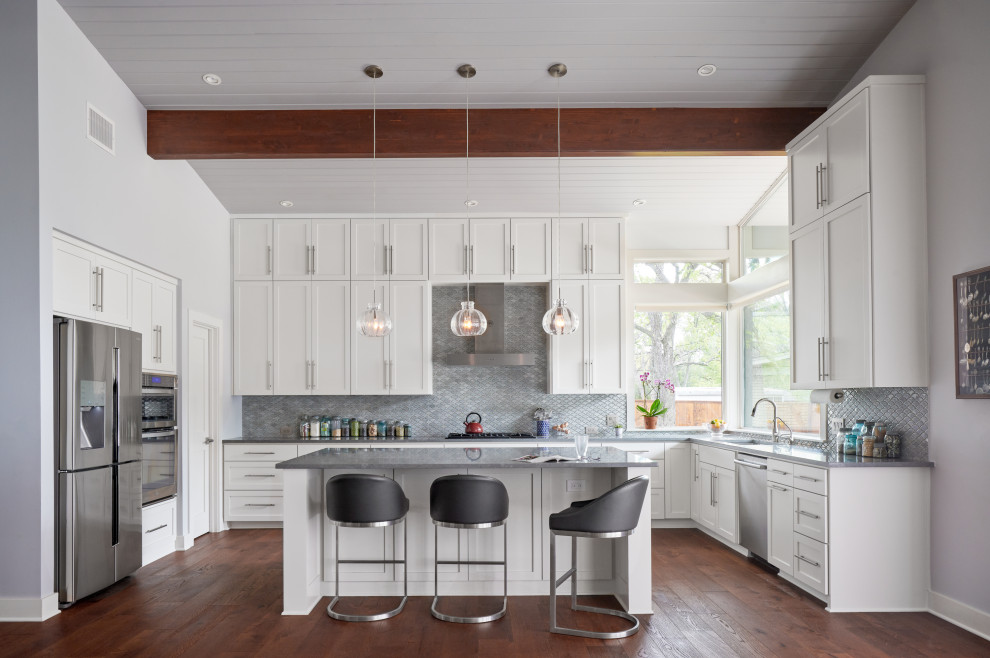 Inspiration for a mid-sized midcentury l-shaped open plan kitchen in Austin with an undermount sink, shaker cabinets, white cabinets, quartz benchtops, grey splashback, ceramic splashback, stainless steel appliances, medium hardwood floors, with island, brown floor, grey benchtop and vaulted.