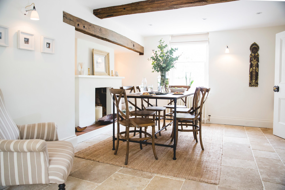 This is an example of a country dining room in London with white walls, a standard fireplace and beige floor.