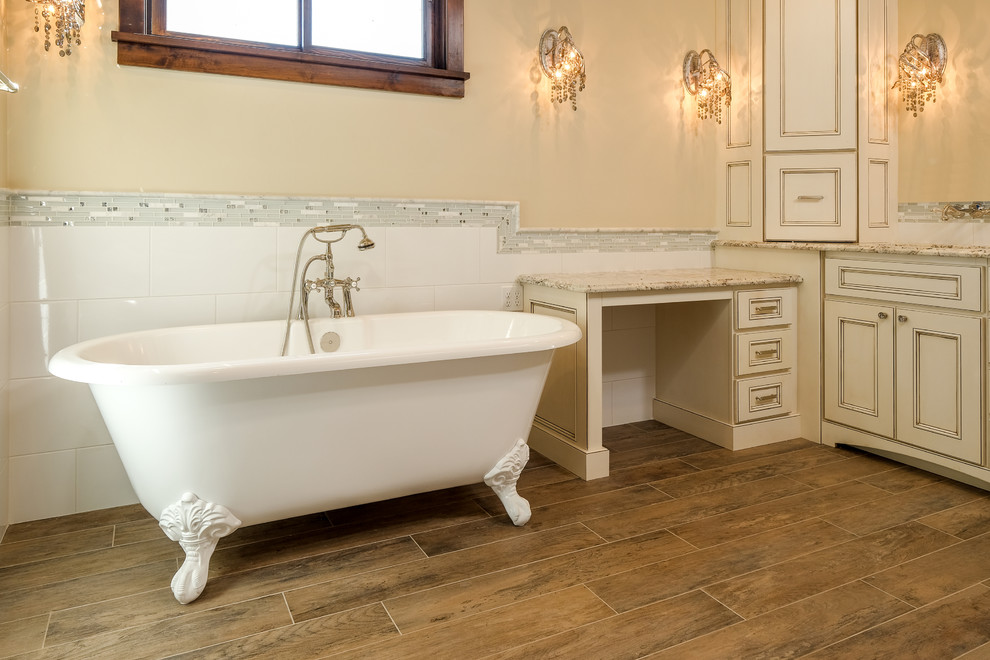 Inspiration for a large country master bathroom in Denver with recessed-panel cabinets, distressed cabinets, a freestanding tub, a two-piece toilet, gray tile, white tile, matchstick tile, beige walls, medium hardwood floors and granite benchtops.