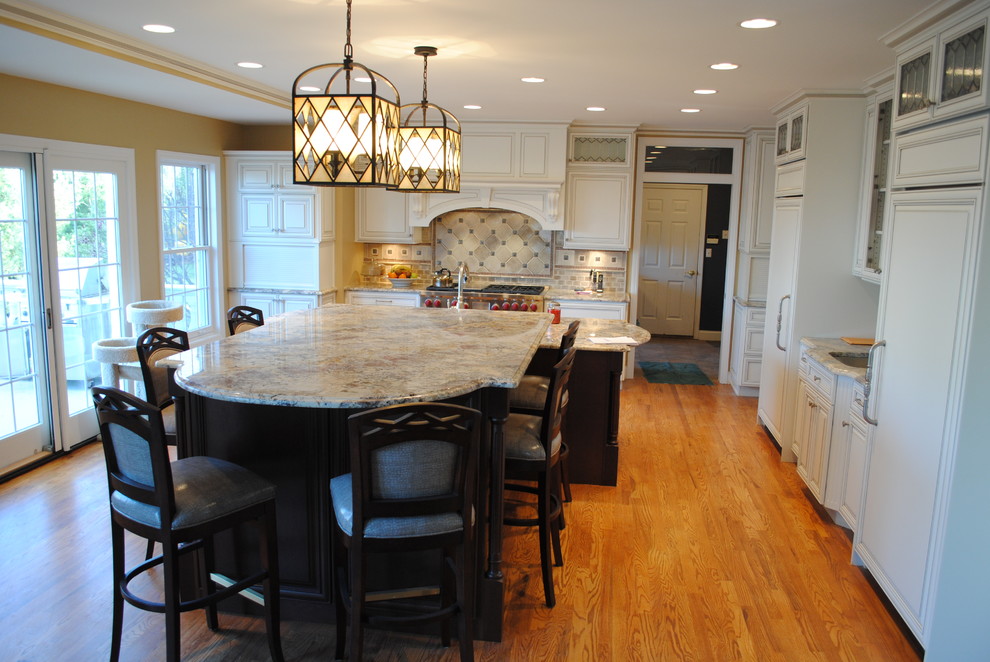 Example of a mid-sized l-shaped medium tone wood floor enclosed kitchen design with a double-bowl sink, raised-panel cabinets, white cabinets, granite countertops, beige backsplash, stone tile backsplash, stainless steel appliances and an island