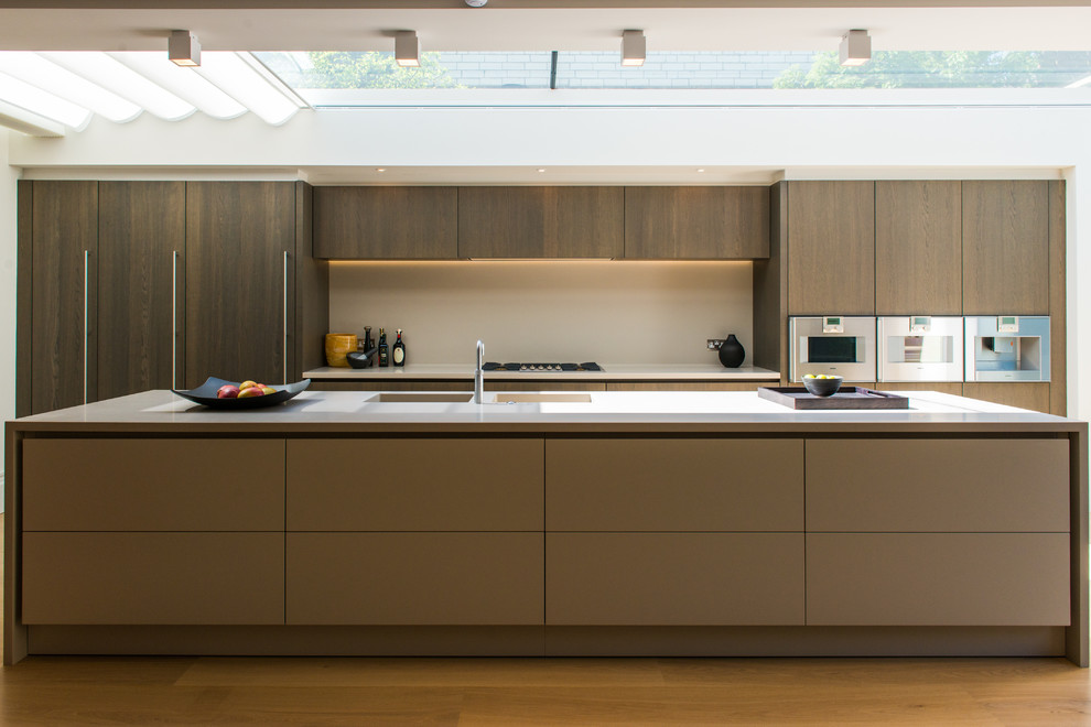Large contemporary galley open plan kitchen in London with a double-bowl sink, flat-panel cabinets, dark wood cabinets, beige splashback, medium hardwood floors, with island and stainless steel appliances.