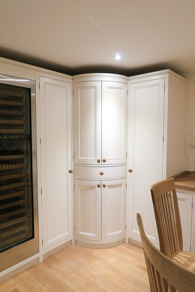 Design ideas for a large traditional l-shaped kitchen in London with a submerged sink, recessed-panel cabinets, white cabinets, wood worktops, stainless steel appliances, medium hardwood flooring and an island.