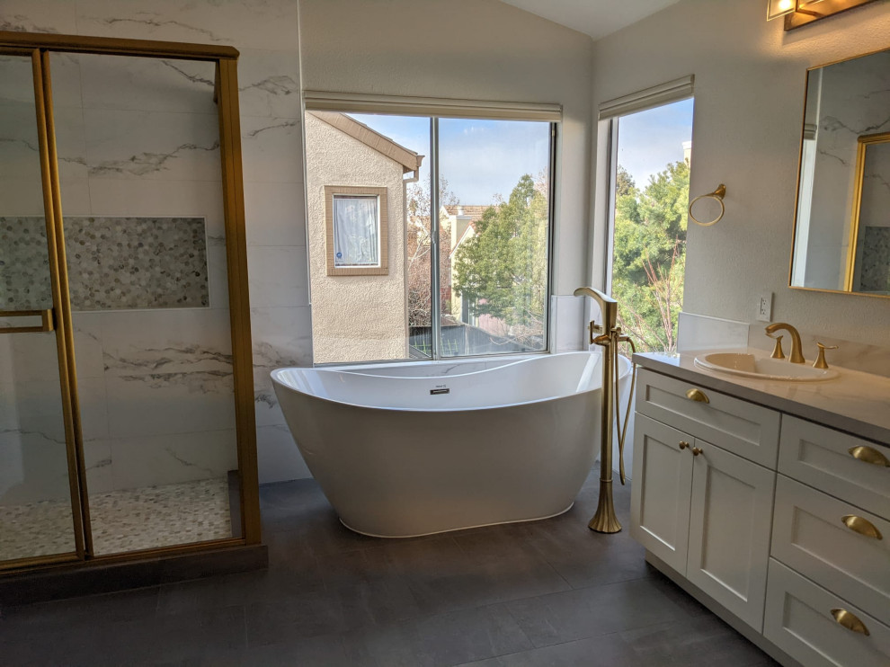 This is an example of a bathroom in San Francisco with raised-panel cabinets, white cabinets, a freestanding tub, a corner shower, a wall-mount toilet, white tile, white walls, an undermount sink, marble benchtops, grey floor, a sliding shower screen, multi-coloured benchtops, a niche, a double vanity and a built-in vanity.