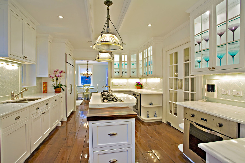 Photo of a traditional separate kitchen in New York with glass-front cabinets, white cabinets, subway tile splashback and panelled appliances.