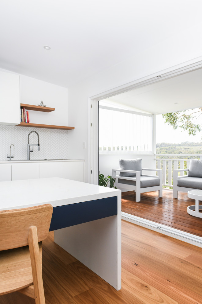 Design ideas for a large contemporary galley open plan kitchen in Sydney with a submerged sink, white cabinets, engineered stone countertops, white splashback, porcelain splashback, integrated appliances, an island, brown floors and white worktops.