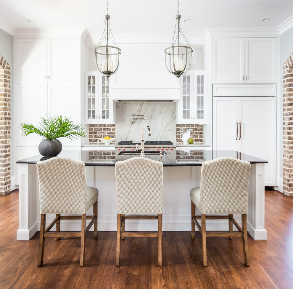 Design ideas for a traditional galley kitchen in Charleston with an undermount sink, recessed-panel cabinets, white cabinets, brown splashback, brick splashback, panelled appliances, dark hardwood floors, with island and brown floor.