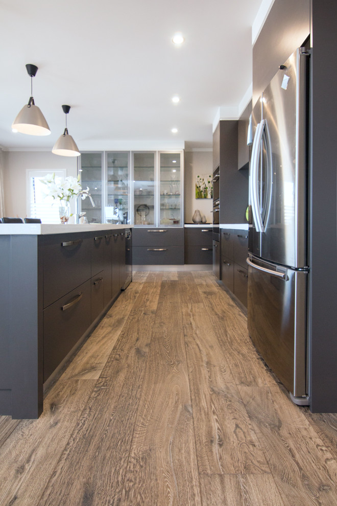Mid-sized country galley eat-in kitchen in Auckland with medium hardwood floors, brown floor, a drop-in sink, flat-panel cabinets, black cabinets, granite benchtops, stainless steel appliances and with island.