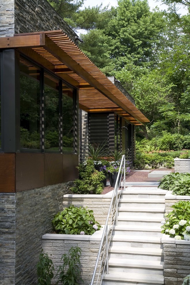 This is an example of a large contemporary one-storey grey exterior in New York with stone veneer and a flat roof.
