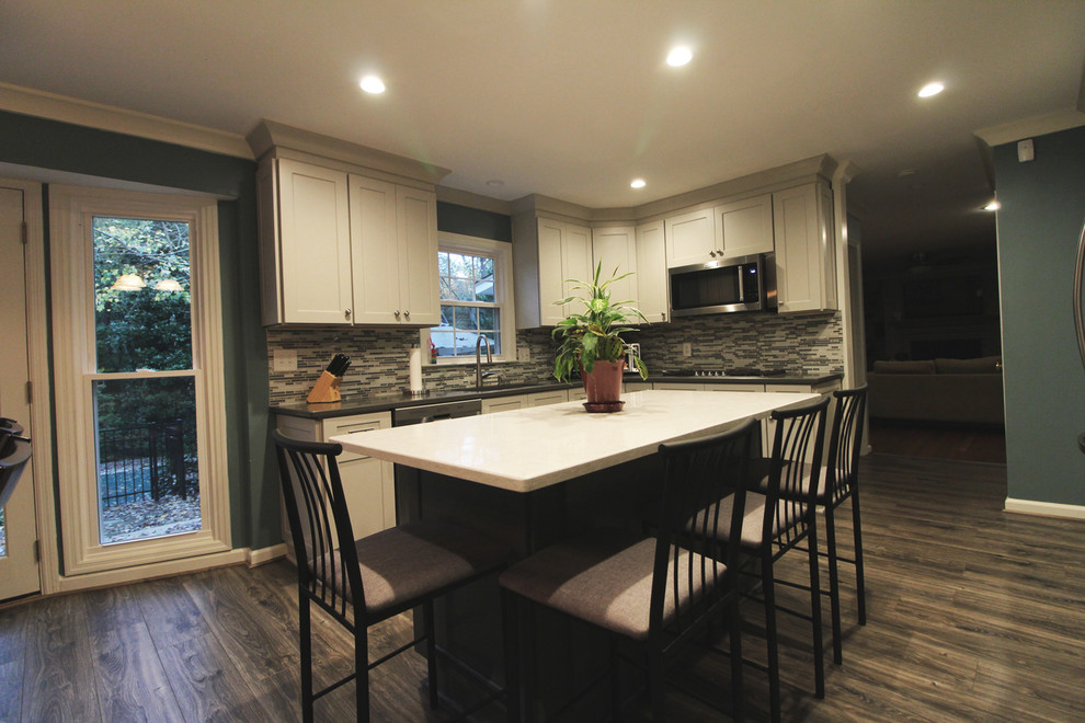 This is an example of a mid-sized transitional u-shaped eat-in kitchen in Atlanta with a drop-in sink, white cabinets, granite benchtops, grey splashback, matchstick tile splashback, stainless steel appliances, medium hardwood floors, with island, brown floor, shaker cabinets and grey benchtop.
