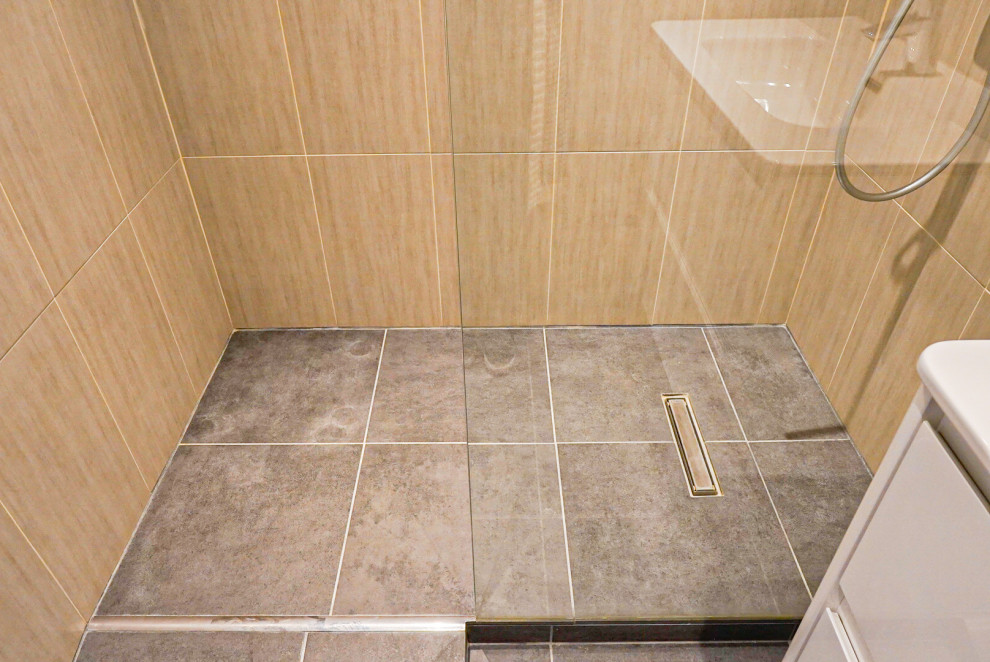 Modern inredning av ett mellanstort brun brunt badrum med dusch, med luckor med infälld panel, beige skåp, våtrum, en vägghängd toalettstol, brun kakel, marmorkakel, bruna väggar, klinkergolv i keramik, ett undermonterad handfat, bänkskiva i akrylsten, grått golv och dusch med gångjärnsdörr