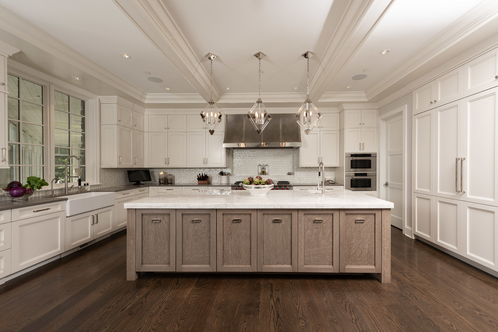 Photo of a large traditional kitchen in Chicago with a farmhouse sink, white cabinets, granite benchtops, white splashback, mosaic tile splashback, stainless steel appliances, with island, brown floor, shaker cabinets, dark hardwood floors and grey benchtop.