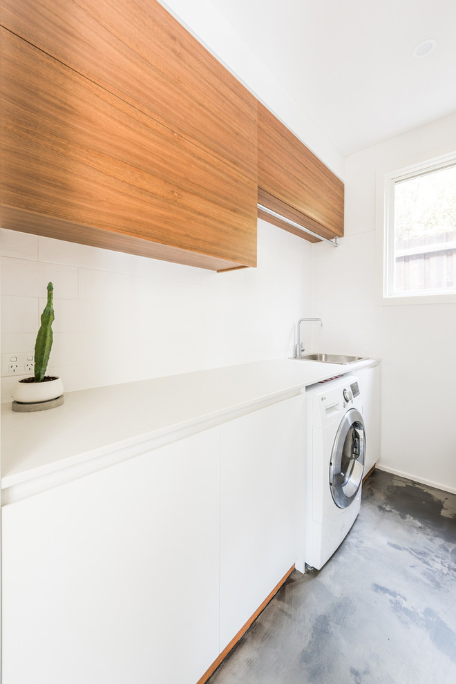 This is an example of a small contemporary single-wall dedicated laundry room in Melbourne with a single-bowl sink, flat-panel cabinets, white cabinets, quartz benchtops, white walls, concrete floors, a side-by-side washer and dryer, grey floor and white benchtop.