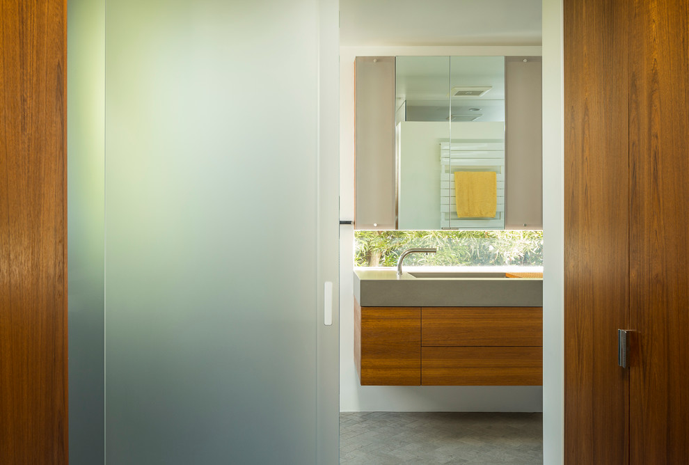 Photo of a mid-sized modern master bathroom in San Francisco with an integrated sink, flat-panel cabinets, medium wood cabinets, concrete benchtops, a curbless shower, a wall-mount toilet, gray tile, porcelain tile, white walls and porcelain floors.