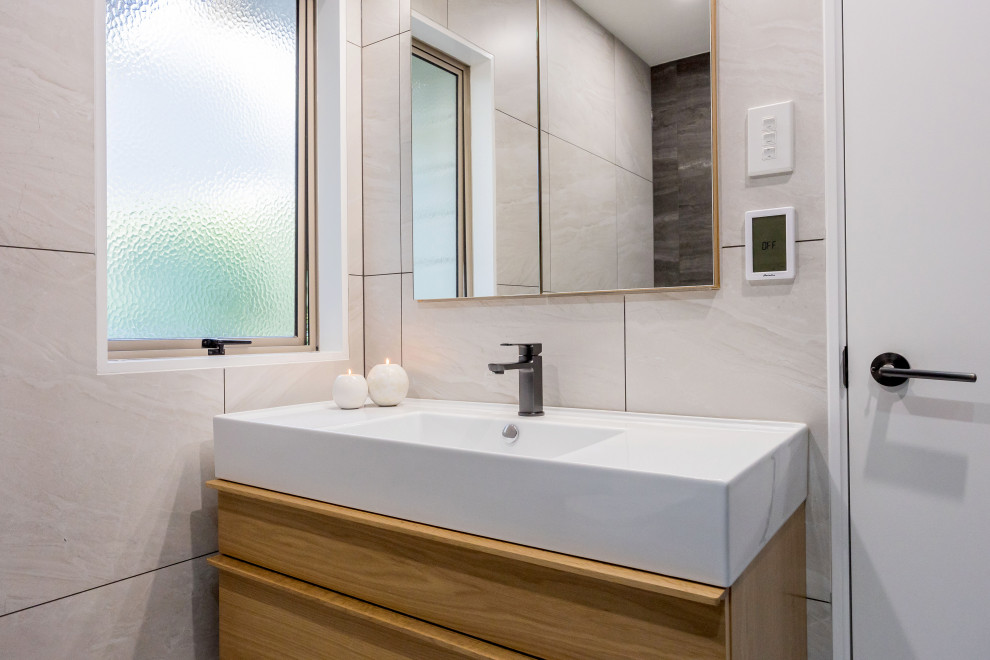 Photo of a small modern 3/4 bathroom in Auckland with light wood cabinets, a freestanding tub, an alcove shower, gray tile, ceramic tile, porcelain floors, an integrated sink, solid surface benchtops, white floor, a hinged shower door, white benchtops, a single vanity and a floating vanity.