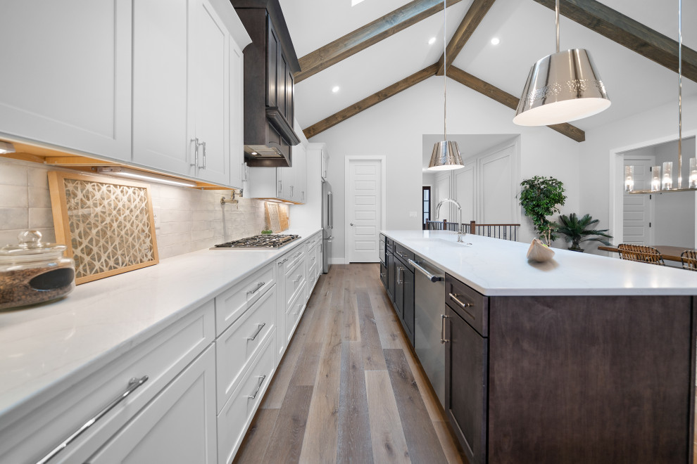 Example of a transitional galley medium tone wood floor and vaulted ceiling open concept kitchen design in Cincinnati with an undermount sink, shaker cabinets, white cabinets, quartz countertops, white backsplash, ceramic backsplash, stainless steel appliances, an island and white countertops