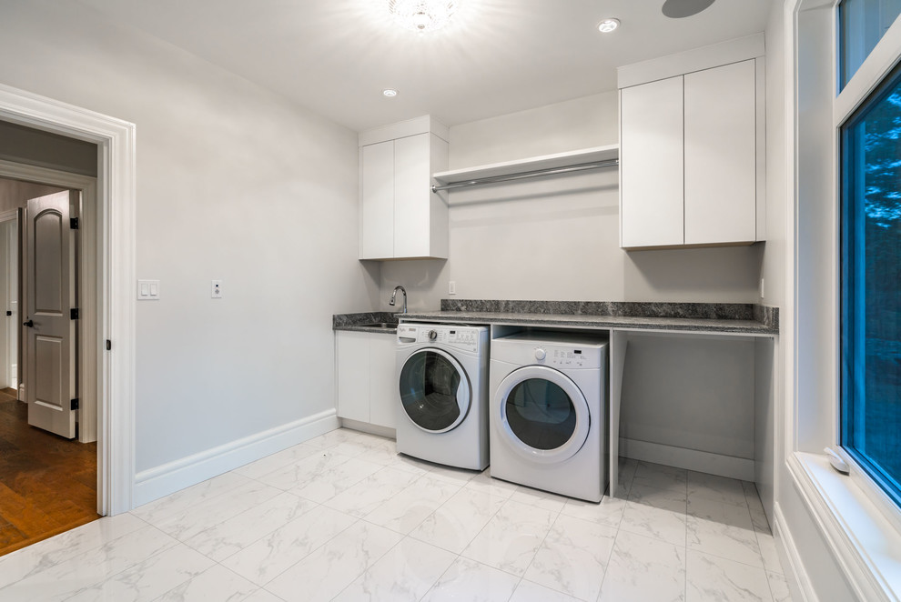 Mid-sized transitional single-wall dedicated laundry room in Other with a drop-in sink, flat-panel cabinets, white cabinets, granite benchtops, grey walls, marble floors, a side-by-side washer and dryer, white floor and grey benchtop.