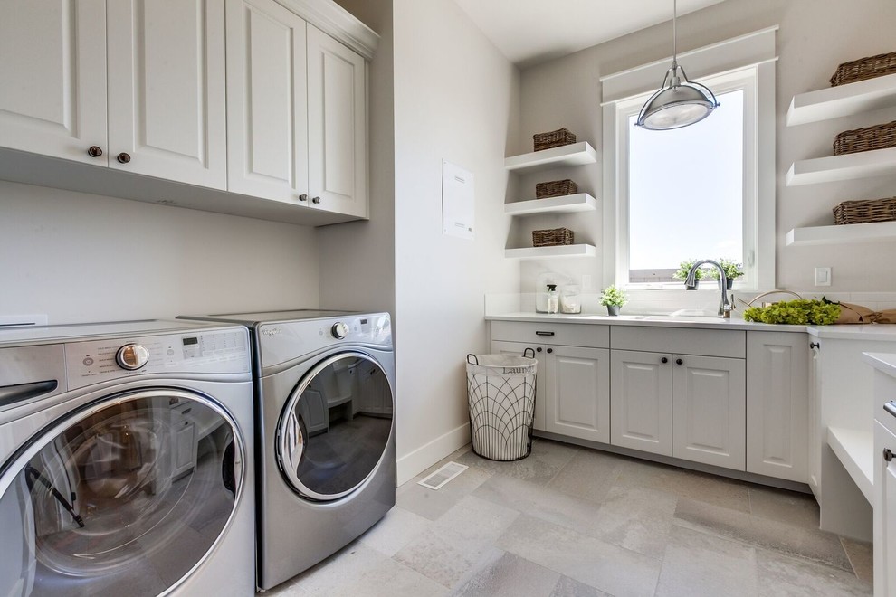 Photo of a large transitional u-shaped utility room in Boise with an undermount sink, raised-panel cabinets, white cabinets, solid surface benchtops, beige walls, porcelain floors, a side-by-side washer and dryer and beige floor.