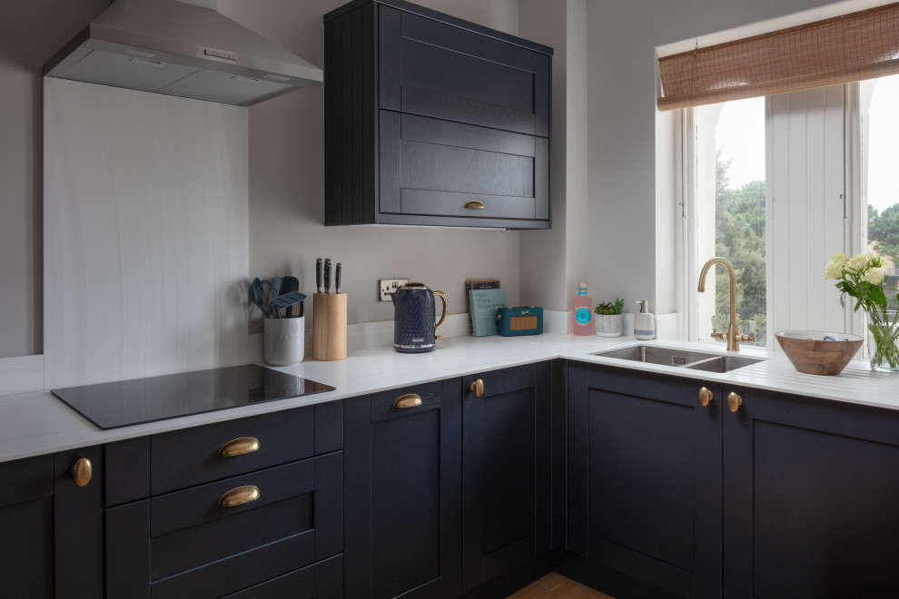 Inspiration for a small coastal u-shaped open plan kitchen in Cornwall with a double-bowl sink, shaker cabinets, blue cabinets, composite countertops, white splashback, engineered quartz splashback, stainless steel appliances, medium hardwood flooring, no island, brown floors and white worktops.