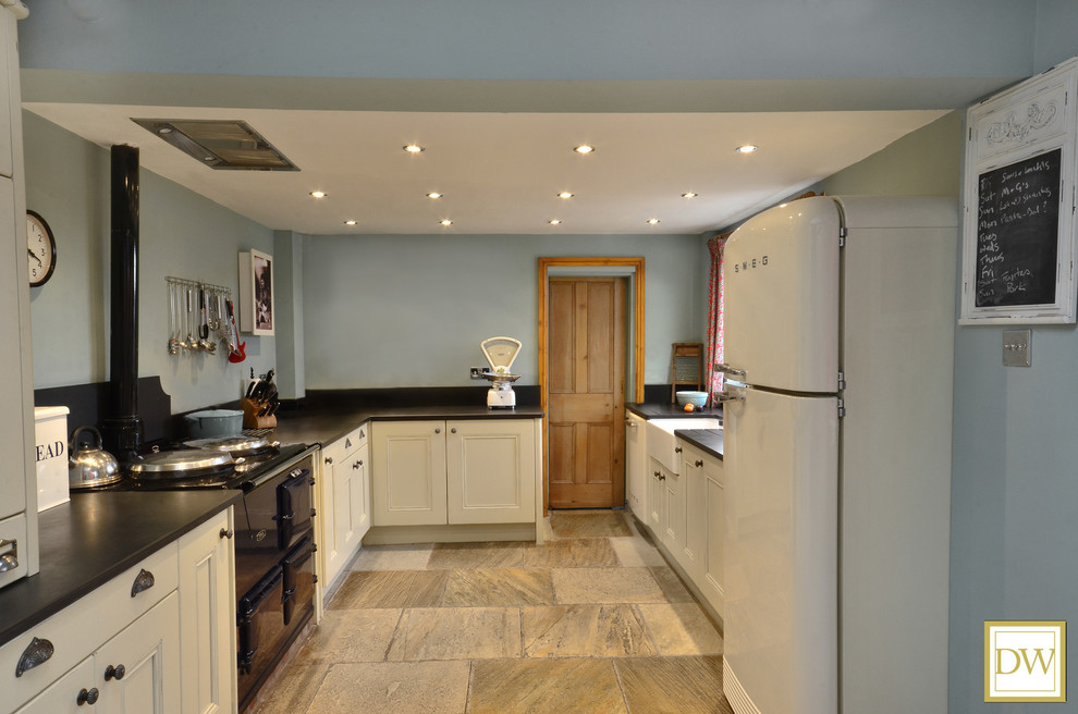 This is an example of a large traditional l-shaped separate kitchen in Other with a farmhouse sink, beaded inset cabinets, beige cabinets, black splashback, slate splashback, coloured appliances, slate floors and beige floor.