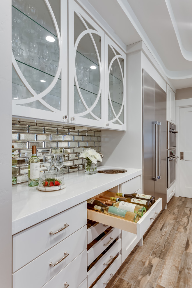 Mid-sized transitional single-wall wet bar in Sacramento with an undermount sink, flat-panel cabinets, white cabinets, solid surface benchtops, mirror splashback, medium hardwood floors, brown floor and white benchtop.