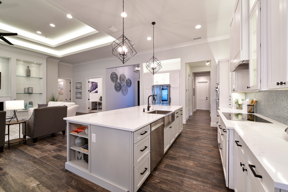 Mid-sized transitional l-shaped porcelain tile and brown floor eat-in kitchen photo with a farmhouse sink, shaker cabinets, white cabinets, quartz countertops, metallic backsplash, glass tile backsplash, stainless steel appliances, an island and white countertops