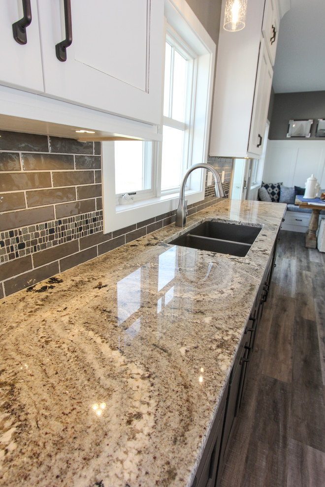 Eat-in kitchen - mid-sized transitional l-shaped laminate floor and brown floor eat-in kitchen idea in Minneapolis with an undermount sink, shaker cabinets, white cabinets, granite countertops, gray backsplash, ceramic backsplash, an island and multicolored countertops