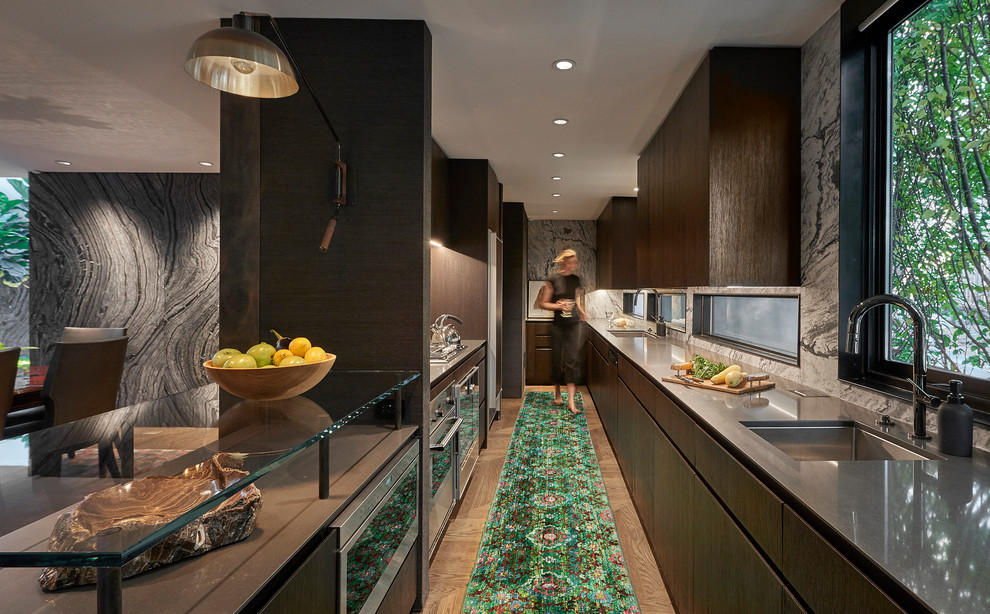 Design ideas for a contemporary galley open plan kitchen in Chicago with an undermount sink, flat-panel cabinets, dark wood cabinets, grey splashback, stone slab splashback, stainless steel appliances, medium hardwood floors, a peninsula, brown floor and grey benchtop.