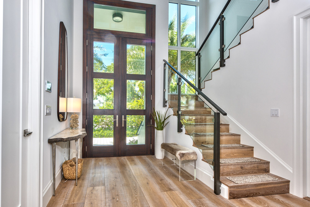 This is an example of a beach style foyer in Miami with white walls, medium hardwood floors, a double front door, a glass front door and brown floor.
