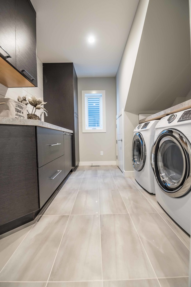 Inspiration for a large industrial galley dedicated laundry room in Calgary with a drop-in sink, flat-panel cabinets, dark wood cabinets, laminate benchtops, grey walls, ceramic floors and a side-by-side washer and dryer.