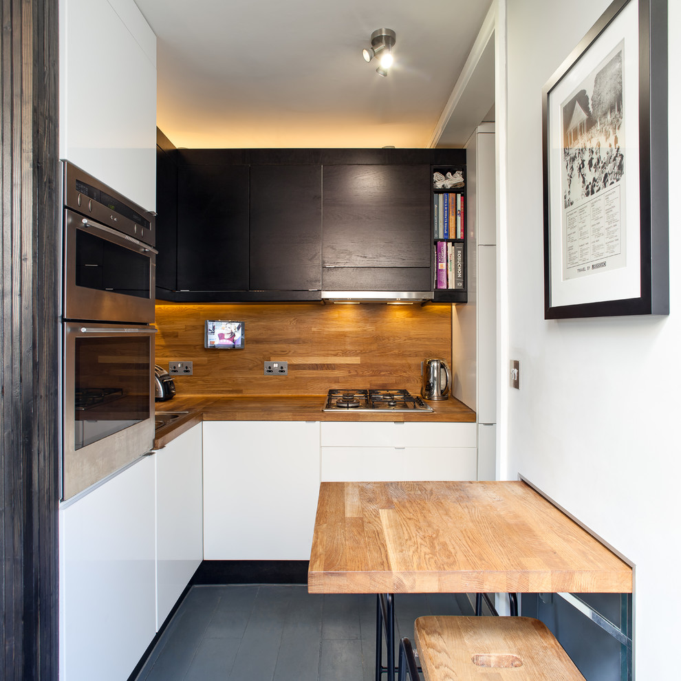 Small contemporary l-shaped open plan kitchen in London with a drop-in sink, flat-panel cabinets, black cabinets, wood benchtops, brown splashback, timber splashback, stainless steel appliances, painted wood floors, a peninsula, grey floor and brown benchtop.