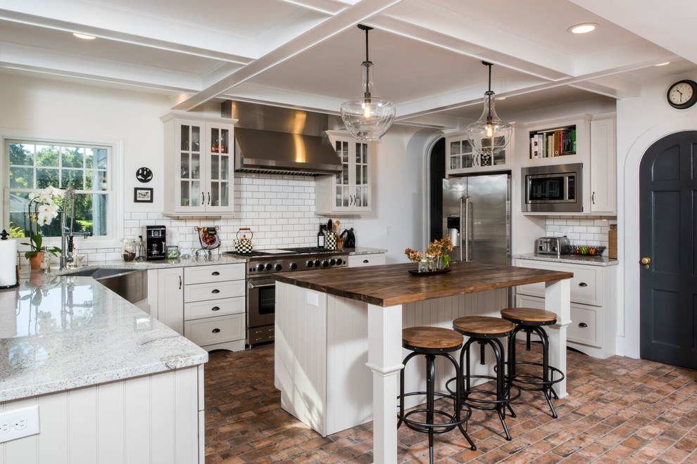 Inspiration for a large country u-shaped kitchen in Other with a farmhouse sink, shaker cabinets, granite benchtops, white splashback, ceramic splashback, stainless steel appliances, brick floors, with island, multi-coloured floor and white cabinets.
