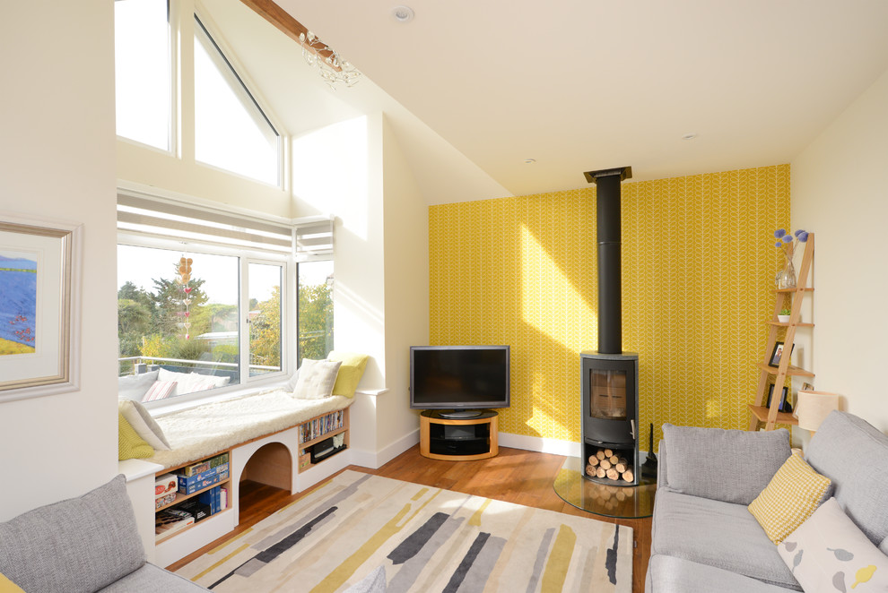 Photo of an eclectic family room in Kent with yellow walls, medium hardwood floors, a wood stove, a metal fireplace surround, a freestanding tv and brown floor.