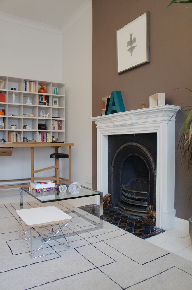 This is an example of a small eclectic formal enclosed living room in London with white walls, light hardwood floors, a standard fireplace, a metal fireplace surround and no tv.