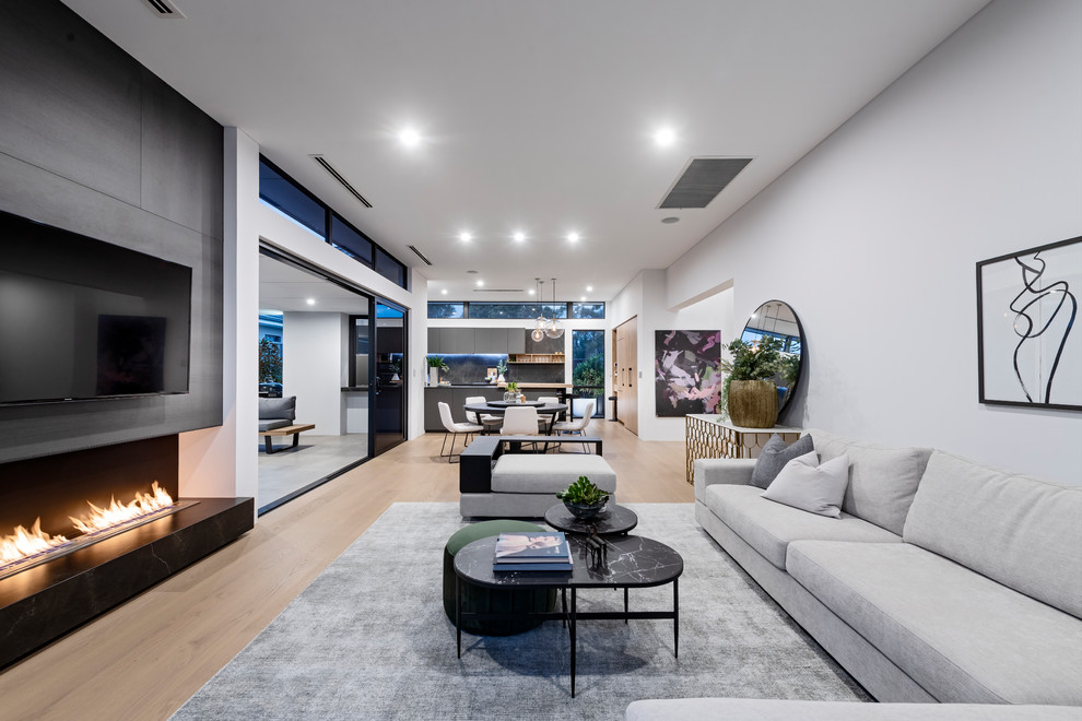 Photo of a contemporary open concept living room in Perth with white walls, light hardwood floors, a ribbon fireplace, a wall-mounted tv and beige floor.