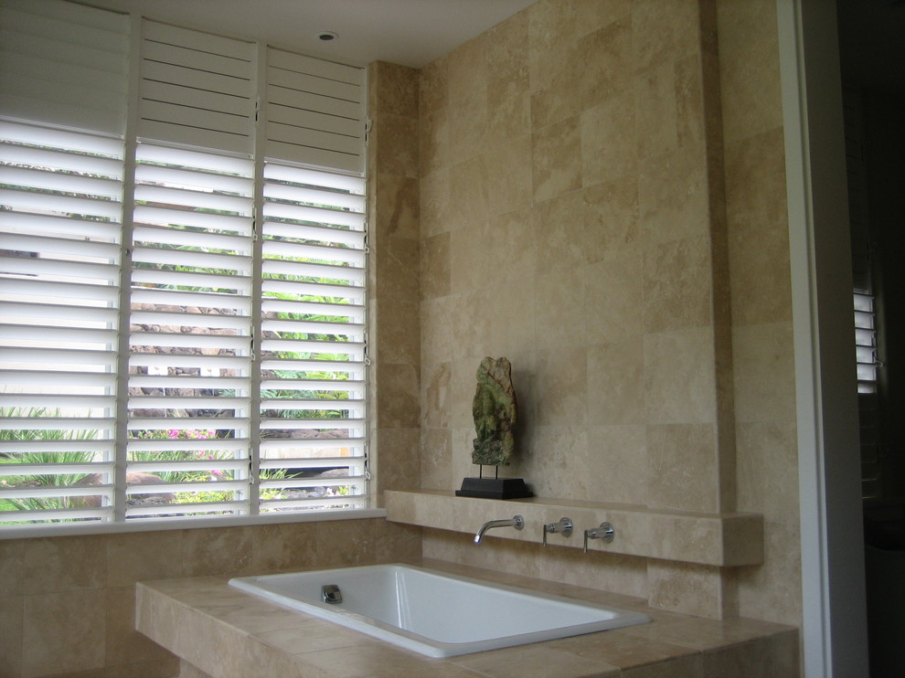 This is an example of a tropical bathroom in Hawaii with a drop-in tub, stone tile and travertine floors.