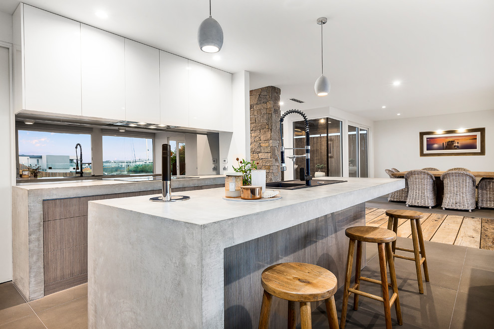 Inspiration for a mid-sized contemporary galley open plan kitchen in Melbourne with light wood cabinets, concrete benchtops, black splashback, limestone floors, with island, grey floor, a single-bowl sink, flat-panel cabinets, grey benchtop and window splashback.