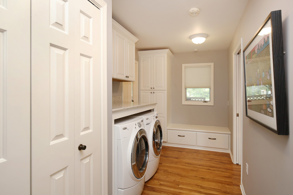 Inspiration for a small traditional galley dedicated laundry room in Grand Rapids with recessed-panel cabinets, quartz benchtops, grey splashback, subway tile splashback, light hardwood floors, white cabinets, grey walls and a side-by-side washer and dryer.