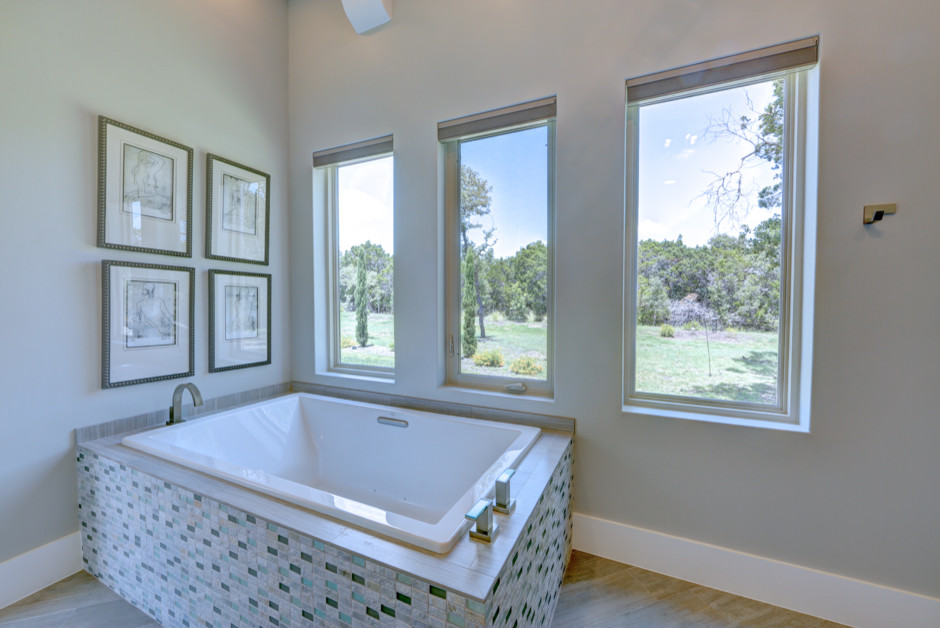 This is an example of a large transitional master bathroom in Austin with granite benchtops, a drop-in tub, gray tile, grey walls, recessed-panel cabinets, grey cabinets, a curbless shower, a two-piece toilet, mosaic tile, medium hardwood floors, an undermount sink, brown floor and a hinged shower door.