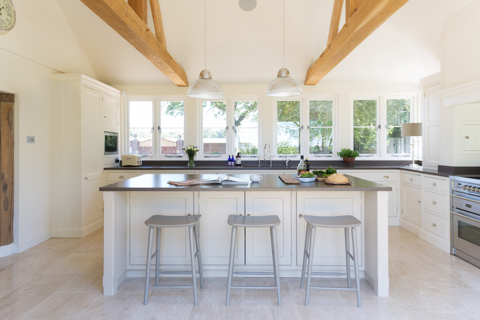 This is an example of a large transitional l-shaped open plan kitchen in Essex with stainless steel appliances, limestone floors, with island, an undermount sink, recessed-panel cabinets and white cabinets.