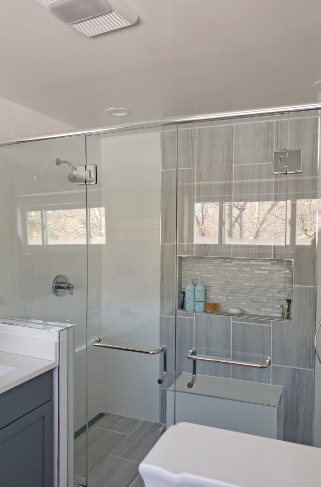 Walk-in shower - large transitional master gray tile and porcelain tile porcelain tile, gray floor and double-sink walk-in shower idea with shaker cabinets, gray cabinets, a two-piece toilet, white walls, an undermount sink, quartz countertops, a hinged shower door, white countertops, a niche and a built-in vanity