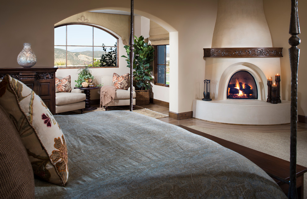 Design ideas for a large mediterranean master bedroom in San Diego with beige walls, light hardwood floors, a corner fireplace and a plaster fireplace surround.